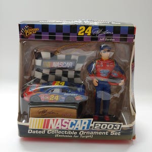 May include: A 2003 NASCAR dated collectible ornament set featuring a Jeff Gordon figure in a red and blue racing suit, a miniature number 24 DuPont race car, and a checkered flag ornament, all housed in a branded cardboard display box.