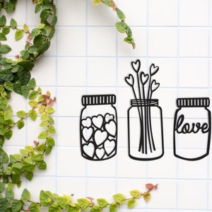 Pode incluir: Três frascos de vidro preto e branco com designs diferentes. O primeiro frasco está cheio de corações, o segundo frasco tem um buquê de flores e o terceiro frasco tem a palavra "love" escrita nele.