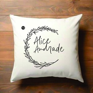 Puede incluir: Almohada blanca con un diseño de corona floral negra y el texto "Alice Andrade" impreso en ella.