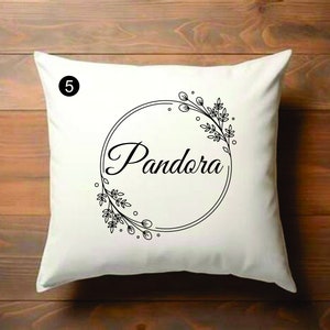 Puede incluir: Almohada blanca con texto negro y diseño floral. El texto dice "Pandora".