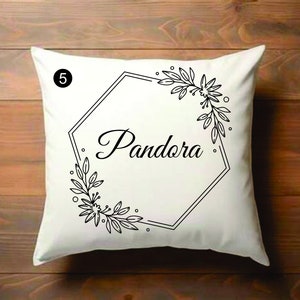 Puede incluir: Almohada blanca con diseño floral negro y un marco hexagonal con la palabra "Pandora" en su interior. El número "5" está en la esquina superior izquierda.
