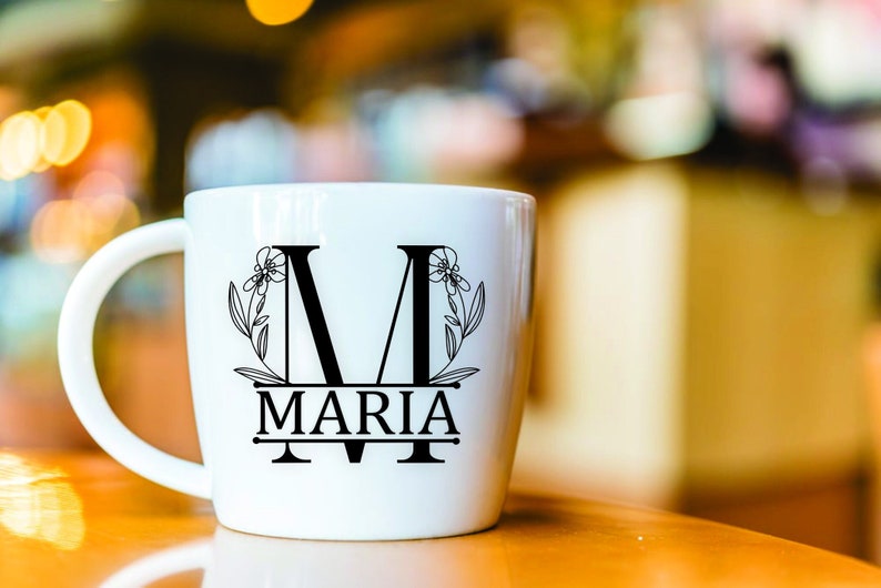 Może przedstawiać: Biały kubek ceramiczny z czarnym wzorem kwiatowym i nadrukowanym imieniem "MARIA".