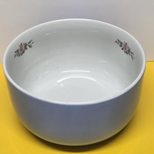 May include: A large, round, ceramic bowl with a light blue exterior and a white interior. The bowl features delicate pink floral accents on the inside rim. The bowl is set against a yellow background.