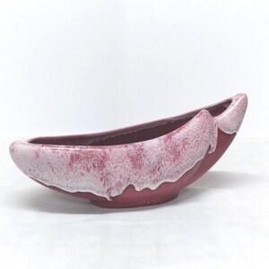 May include: A vintage, boat-shaped ceramic planter in shades of red and pink. The planter has a smooth, glossy finish with a lighter pink, speckled glaze along the rim, creating a unique, decorative piece.