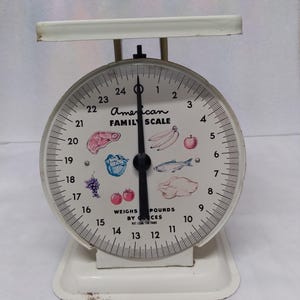 May include: White vintage kitchen scale with a round dial that reads up to 24 pounds. The dial has illustrations of various foods, including a steak, bananas, an apple, grapes, tomatoes, fish, and chicken. The scale reads "American Family Scale" and "Weighs by Ounces".