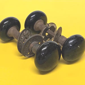 May include: A collection of vintage black door knobs with aged metal hardware. The knobs have a glossy, oval shape and are arranged against a bright yellow background. The hardware shows signs of age and wear.