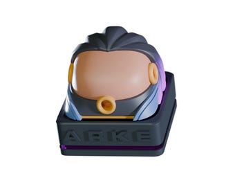 May include: A stylized, futuristic keycap featuring a helmet design. The keycap has a dark gray base with the letters "ABKE" and a purple accent. The helmet is a mix of gray, tan, and blue, with gold-colored circular accents.