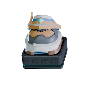 Op de afbeelding: Een gestileerde, futuristische robotkop in tinten grijs, wit en bruin, met blauwe accenten. De robotkop staat op een zwarte rechthoekige basis met het woord "ARKE" op de voorkant. Een kleine antenne steekt uit de bovenkant.