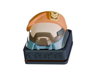 May include: A detailed, orange and blue helmet-shaped object with the word "ARKE" on the base. The helmet has a visor and a small emblem. The base is dark gray.