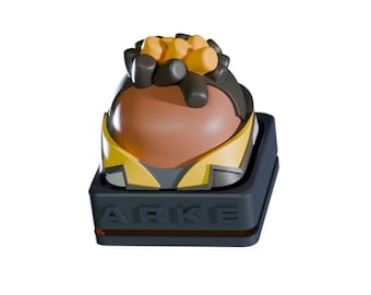 May include: A stylized, two-tone keycap with a brown, rounded top and yellow and gray accents. The keycap is set on a dark gray base with the word "ARKE" printed on the front.