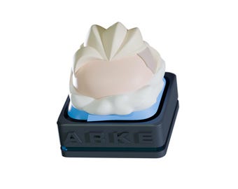 May include: A stylized, abstract sculpture featuring a light pink and white form atop a dark gray rectangular base. The base has the letters "ABKE" on the front. The sculpture has a modern, minimalist aesthetic.
