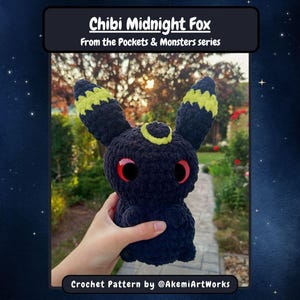 Pode incluir: Um peluche de raposa de crochê azul escuro feito à mão com detalhes amarelos nas orelhas e um anel amarelo na testa. O peluche tem olhos vermelhos grandes. O texto "Chibi Midnight Fox" e "From the Pockets & Monsters series" são exibidos acima do peluche. O texto "Crochet Pattern by @AkemiArtWorks" é exibido abaixo.