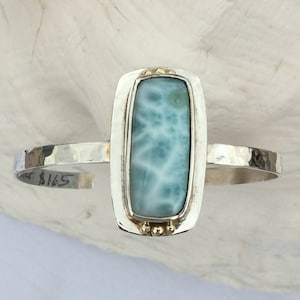 May include: A silver cuff bracelet featuring a rectangular blue and white gemstone set in a gold bezel. The bracelet has a hammered finish and is marked with the number "5165".