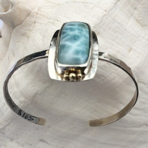 May include: A silver cuff bracelet featuring a rectangular blue and white gemstone set in a silver frame. The bracelet is stamped with the number "B165".
