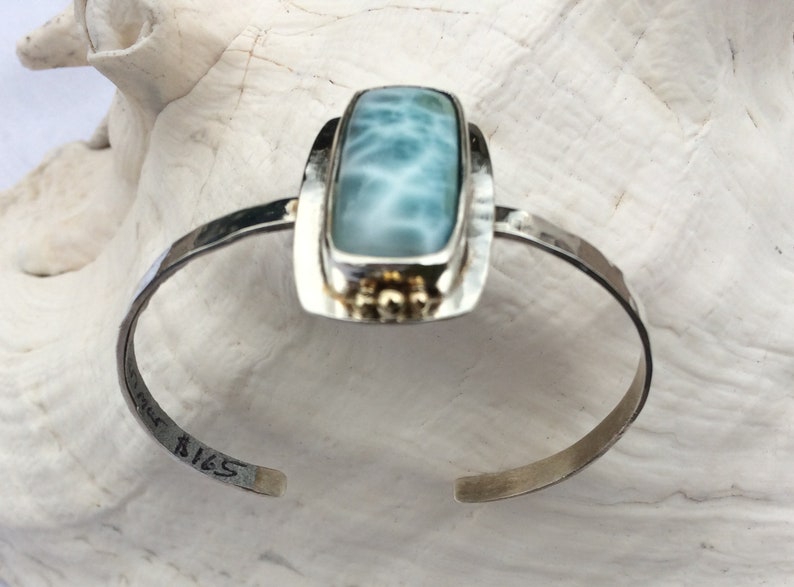 May include: A silver cuff bracelet featuring a rectangular blue and white gemstone set in a silver frame. The bracelet is stamped with the number "B165".