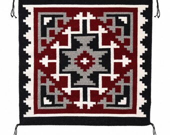 May include: A square woven textile wall hanging featuring a geometric pattern in deep red, black, white, and gray. The design consists of concentric stepped shapes and a central cross motif, finished with small black tassels at each of the four corners.