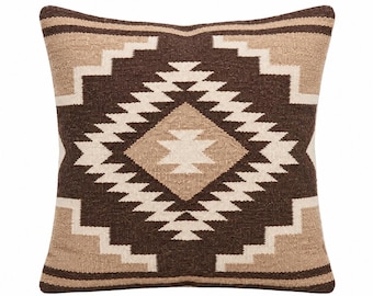 Puede incluir: Un cojín cuadrado con un patrón geométrico tejido en tonos marrón oscuro, beige y crema. El diseño consiste en una gran forma de diamante central rodeada por bordes en zigzag escalonados, con rayas horizontales en la parte superior e inferior.