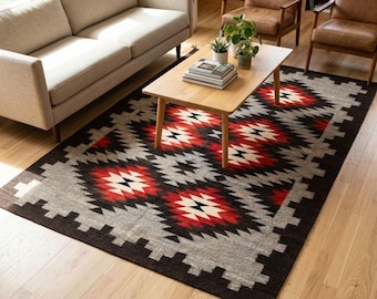 May include: A rectangular area rug featuring a repeating geometric pattern in shades of red, black, white, and gray. The design consists of interconnected diamond shapes with serrated edges, finished with small tassels at the corners.