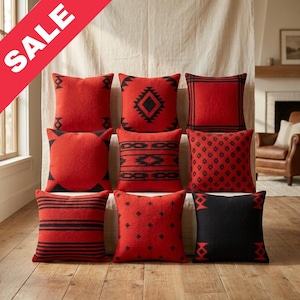 May include: Nine red throw pillows with various black geometric patterns are arranged in a grid. The pillows have different designs, including diamonds, stripes, and crosses. The pillows are displayed on a wooden floor with a neutral backdrop.