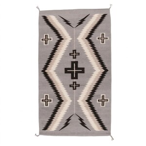 Puede incluir: Alfombra rectangular gris con un dise&ntilde;o geom&eacute;trico. La alfombra presenta una forma de diamante central con zigzags negros, blancos y beige, y cruces negras. La alfombra tiene flecos en los extremos y es adecuada para una sala de estar o dormitorio.