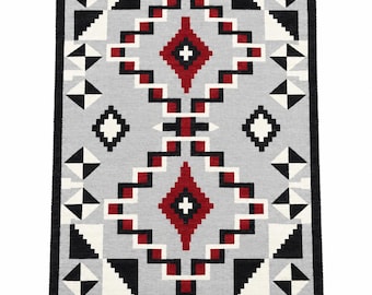 May include: A rectangular area rug featuring a light gray background with a geometric pattern in black, white, and red. The design consists of two large central diamond shapes composed of stepped lines, surrounded by smaller triangles and squares.