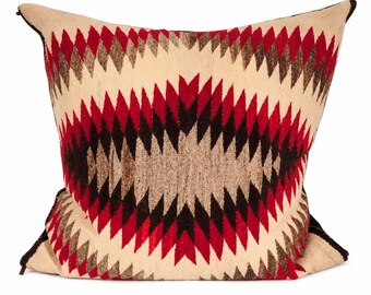 May include: A square throw pillow featuring a woven geometric pattern in cream, deep red, dark brown, and tan. The design consists of concentric diamond shapes radiating from the center, finished with dark brown piping along the outer edges.