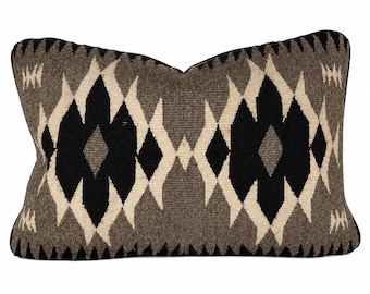 May include: A rectangular throw pillow featuring a woven geometric pattern in black, cream, and shades of gray. The design consists of repeating diamond and zigzag shapes across the entire surface, finished with a solid black piped edge.