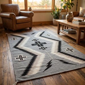 Puede incluir: Una alfombra gris rectangular con un patr&oacute;n geom&eacute;trico de zigzags y cruces negros, blancos y grises. La alfombra est&aacute; colocada sobre un suelo de madera en un sal&oacute;n. El dise&ntilde;o incorpora formas de rel&aacute;mpagos. La alfombra es probablemente de lana.