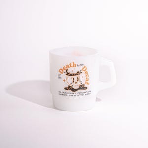 Könnte beinhalten: Weißer Keramikbecher mit Henkel, mit dem Text "Death before Decaf" in Orange, zusammen mit einer Totenkopf-Illustration. Der Becher enthält auch den Text "You only live once, caffeinate and celebrate. Life is better buzzed."