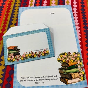 Könnte beinhalten: Ein Schreibwarenset mit blau-weiß kariertem Rand. Das Set enthält einen Umschlag und zwei Blatt Papier. Das Papier trägt den Text "Glücklich sind, die sich ihrer geistigen Not bewusst sind, denn ihnen gehört das Himmelreich." Matthäus 5,3.