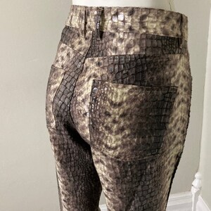 May include: A pair of brown and tan faux snakeskin pants. The pants have a classic five-pocket design with a button and zipper closure. The faux snakeskin pattern is detailed and realistic, with a textured appearance.