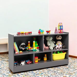 May include: A grey wooden toy storage shelf with six compartments. The shelf is filled with various toys, including stuffed animals, toy cars, building blocks, and books.