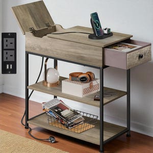 May include: A wooden side table with a lift-top, drawer, and two shelves. It has a black metal frame and includes a wireless charging station with a phone and smartwatch. The table also features a power outlet with two sockets and two USB ports.