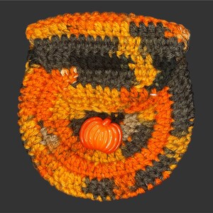 Puede incluir: Una bolsa de crochet con un botón en forma de calabaza en colores naranja y marrón.