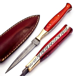 May include: A handcrafted dagger with a Damascus steel blade and a red wooden handle. The handle is accented with brass and decorative silver inlays. A brown leather sheath is included.