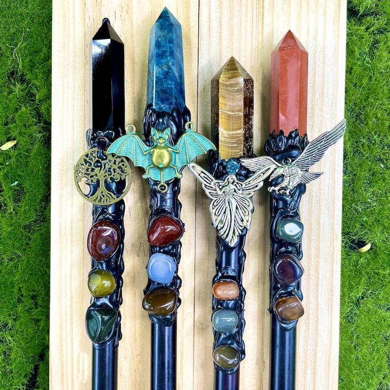 May include: Four black wands with different crystal tops and charms. The wands are decorated with various colored stones. The charms include a tree of life, a bat, a fairy, and an eagle.