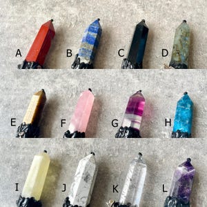 May include: Twelve different crystal point pendants with black metal bases. The crystals are in various colors, including red, blue, black, grey, brown, pink, purple, teal, white, and amethyst.