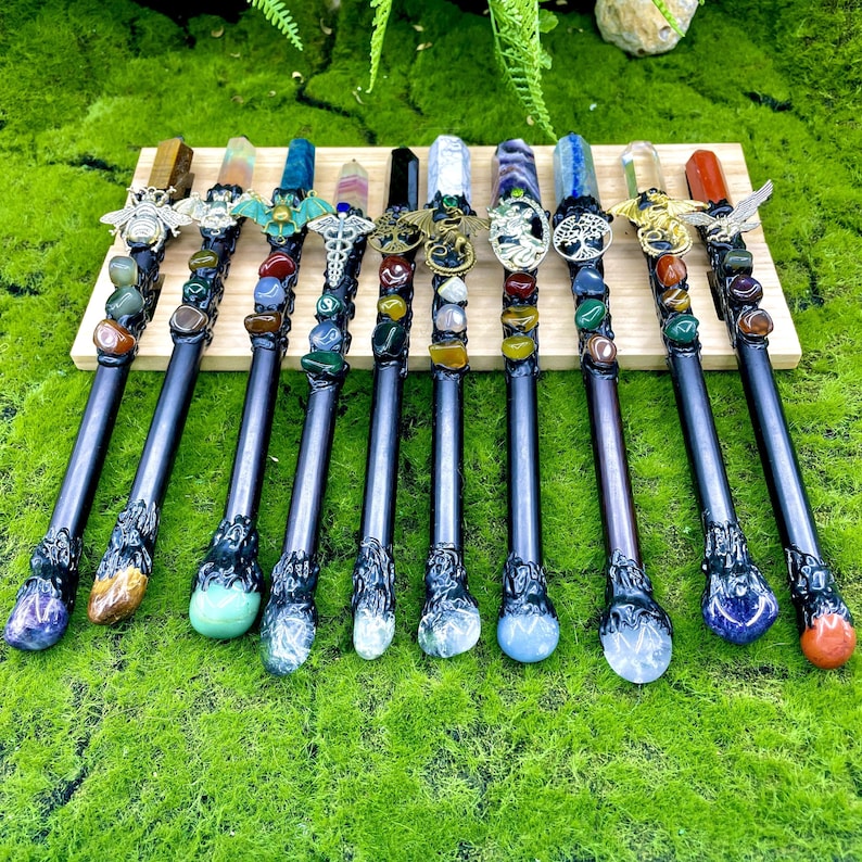 May include: Twelve black wands with different colored crystal tips and decorative metal accents. Each wand is adorned with various gemstones and crystals.