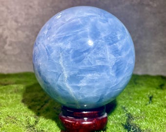May include: A light blue Celestite sphere on a wooden stand. The sphere has a smooth, polished surface with a swirling pattern.