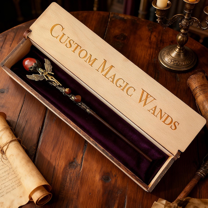 K&ouml;nnte beinhalten: Eine individuelle Zauberstab in einer offenen Holzkiste. Der Zauberstab hat einen roten Edelstein und eine goldfarbene Feenfigur. Das Innere der Box ist mit violettem Samt ausgekleidet. Auf dem Deckel steht "Custom Magic Wands".