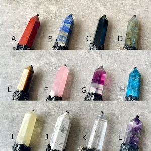 May include: Twelve different crystal point pendants with black metal bases. The crystals are in various colors, including red, blue, black, grey, brown, pink, purple, teal, white, and amethyst.