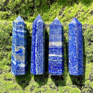 Può includere: Quattro punte di cristallo di lapislazzuli blu con macchie dorate. Le punte sono disposte in fila su un letto di muschio verde.