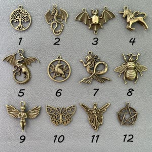 K&ouml;nnte beinhalten: Eine Sammlung antiker, messingfarbener Anh&auml;nger mit verschiedenen Designs. Enth&auml;lt einen Lebensbaum, Drachen, eine Fledermaus, ein Einhorn, eine Meerjungfrau, eine Biene, einen Engel, einen Schmetterling und ein Pentagramm. Jeder Anh&auml;nger hat eine Schlaufe.
