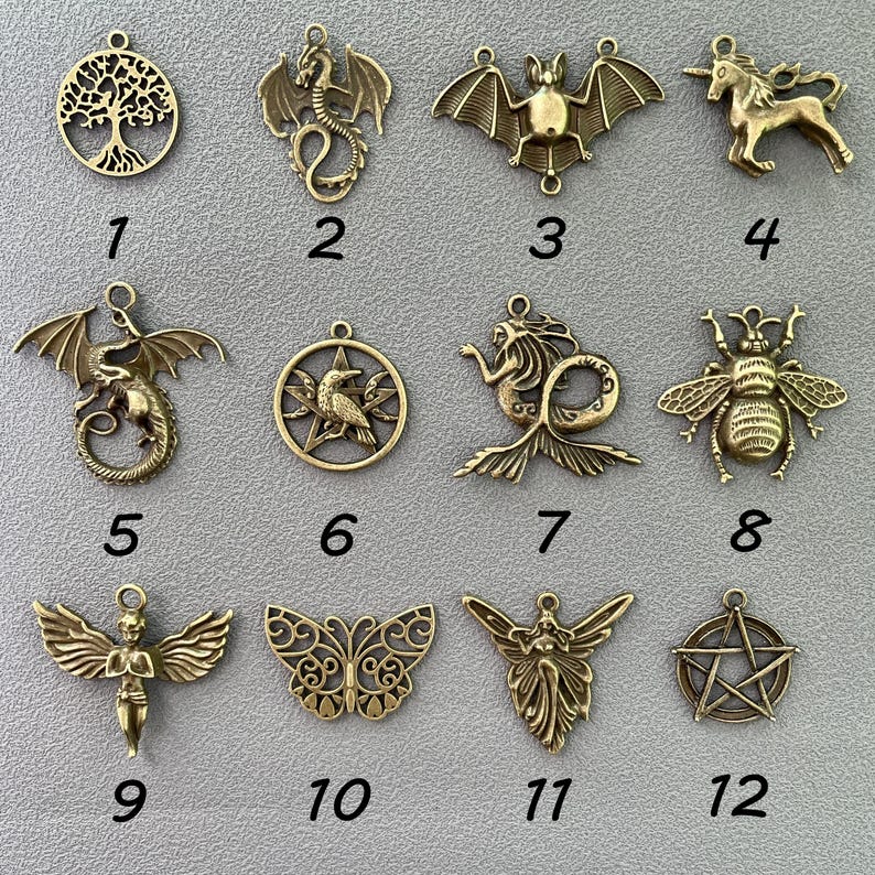 K&ouml;nnte beinhalten: Eine Sammlung antiker, messingfarbener Anh&auml;nger mit verschiedenen Designs. Enth&auml;lt einen Lebensbaum, Drachen, eine Fledermaus, ein Einhorn, eine Meerjungfrau, eine Biene, einen Engel, einen Schmetterling und ein Pentagramm. Jeder Anh&auml;nger hat eine Schlaufe.