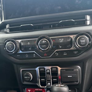 Könnte beinhalten: Nahaufnahme eines Armaturenbretts eines Autos mit Klimaanlagenknöpfen und -tasten. Die Mittelkonsole umfasst Bedienelemente für Klimaanlage, Lüftergeschwindigkeit und Temperatur. Das Armaturenbrett hat auch ein Medienbedienfeld und einen Schalthebel.