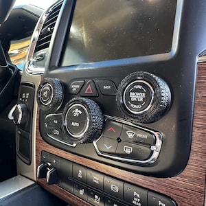 May include: Car dashboard with custom tire-shaped knobs. The dashboard has a large screen, buttons, and controls. The knobs are designed to fit over existing controls. The dashboard has a wood grain finish.