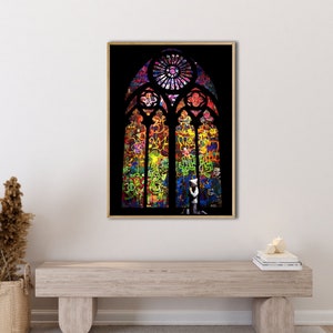 Op de afbeelding: Een kleurrijk glas-in-loodraam met graffitikunst. Het raam is ingelijst in een donkerhouten lijst en staat tegen een witte muur.