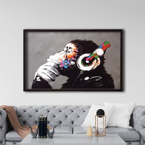 May include: A framed painting of a chimpanzee wearing headphones. The chimpanzee is sitting with its hand on its chin, looking thoughtful. The headphones are colorful and have a red, green, blue, and yellow design. The background is a gray color.