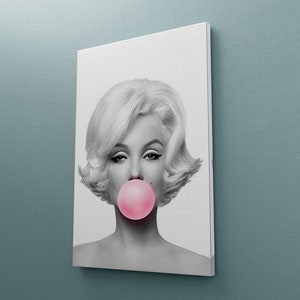 May include: Black and white portrait of a woman with blonde hair blowing a pink bubble. The background is white.