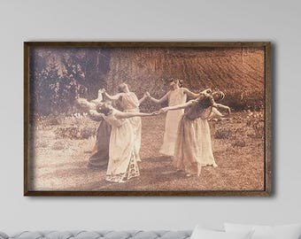 May include: A rectangular framed wall art print featuring a sepia-toned photograph of five figures in long, flowing dresses standing in a circle outdoors, holding hands and looking upward in a grassy field with trees in the background.